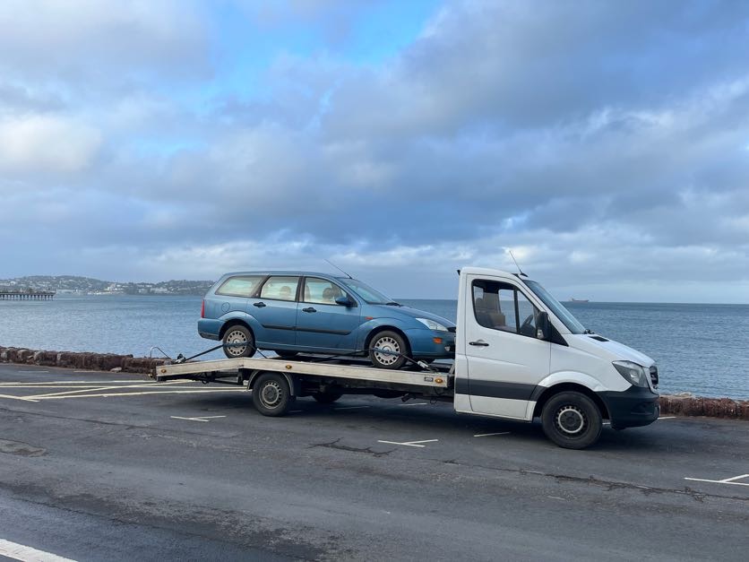 Blue estate car on the AL Services car transporter by the coast